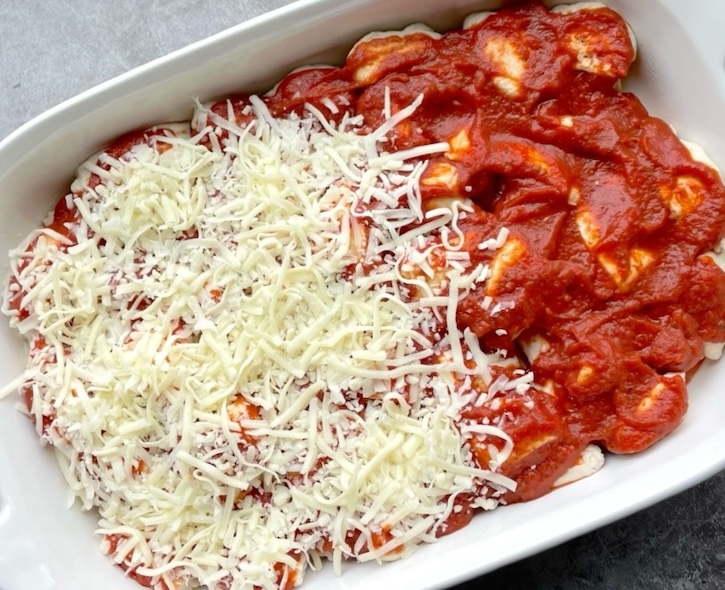 A pizza casserole being prepared for the oven including quartered biscuit dough, sauce and shredded cheese. 