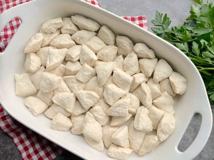 Biscuit dough on the bottom of a 9x13 baking dish ready to be smothered in pizza sauce and shredded mozzarella to make an easy pizza casserole for dinner. 