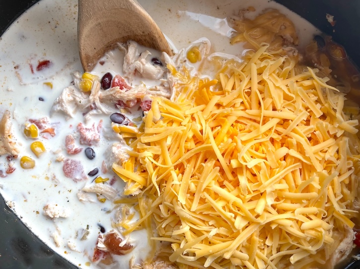 Heavy whipping cream and cheddar cheese in a slow cooker with chicken taco soup just before mixing. 