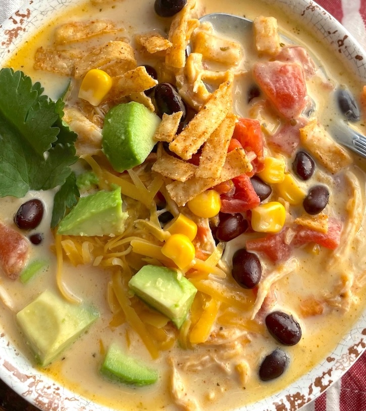 Close up of yummy and creamy chicken taco soup garnished with fresh avocado, cilantro and tortilla chips. 