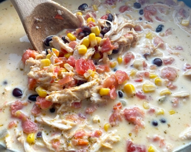 Creamy chicken taco tortilla soup in a slow cooker being mixed with a spoon. 