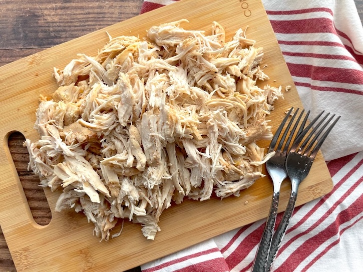 Shredded chicken breasts on a cutting board with forks. 