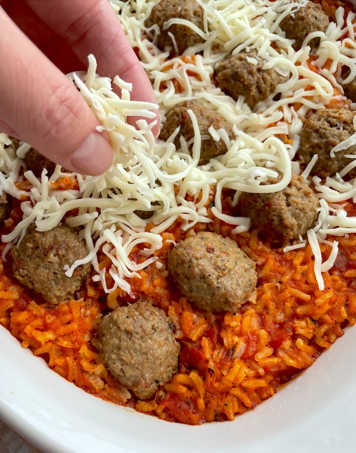 Shredded mozzarella cheese being sprinkled on top of a tasty meatball casserole and rice casserole.