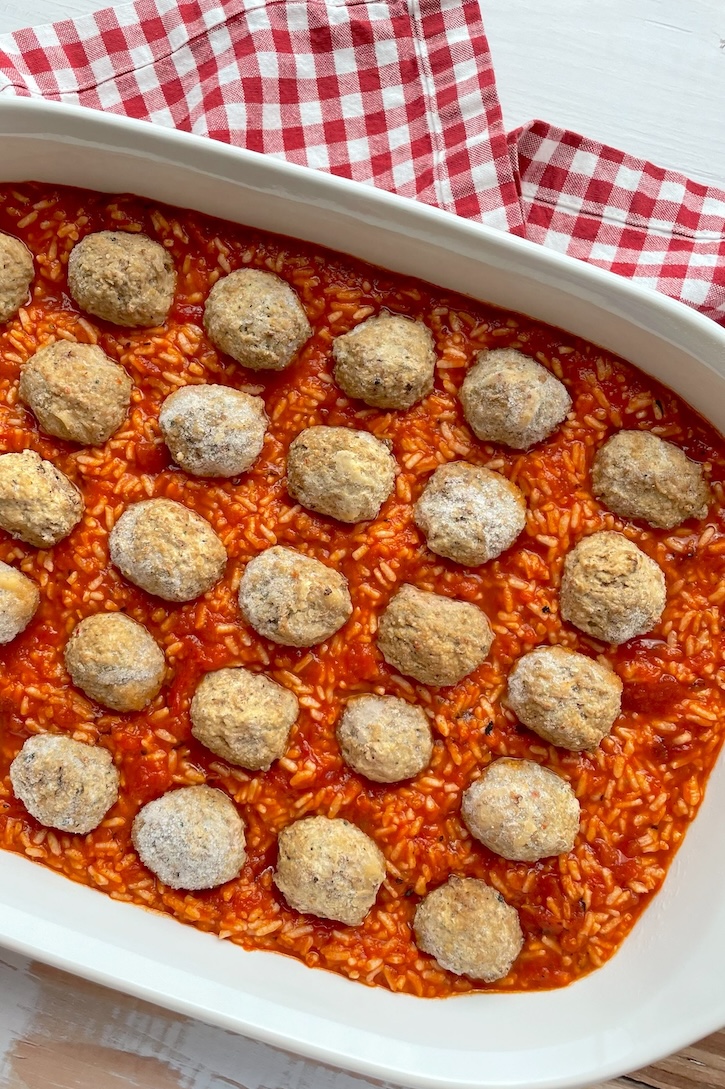 A yummy rice mixture on the bottom of a large baking dish topped with frozen meatballs, ready for the oven to make a cheesy meatball casserole!