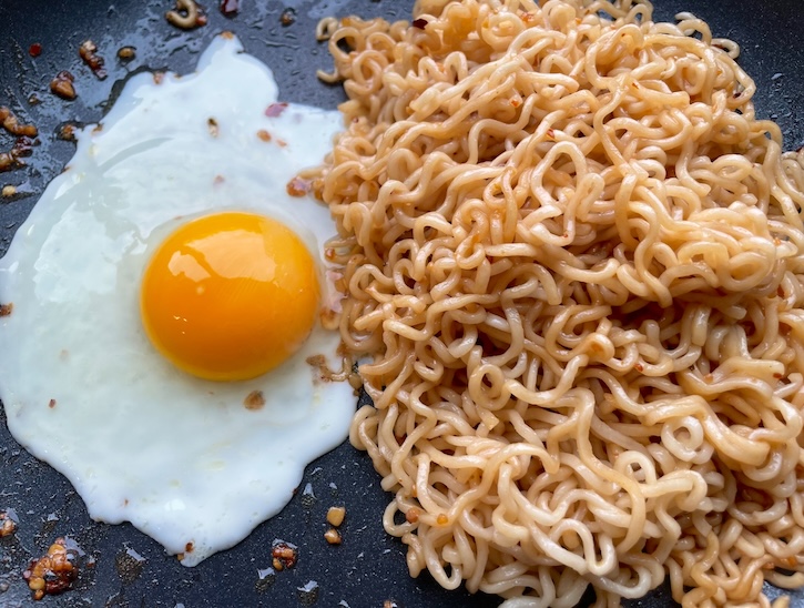 Sweet and spicy garlic ramen noodles in a pan with an egg ready to be mixed to make a quick vegetarian lunch or dinner. 