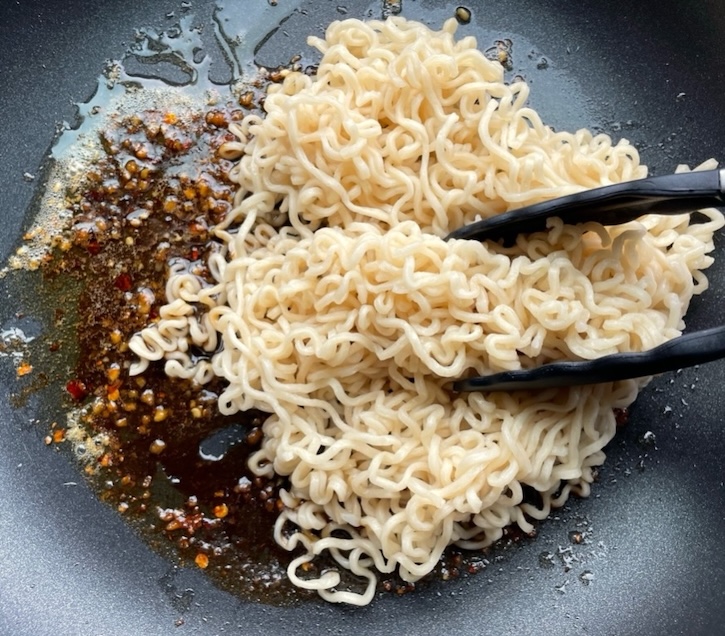 Cooked ramen noodles in a pan being tossed with a homemade sweet and spicy sauce to make a delicious stir fry for dinner. 