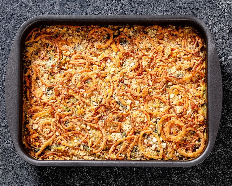 Green bean casserole in a lare dish topped with crispy French fried onions and parmesan cheese. This green bean casserole is improved from the classic with a jar of Alfredo sauce instead of your typical can of soup. No mushrooms! 