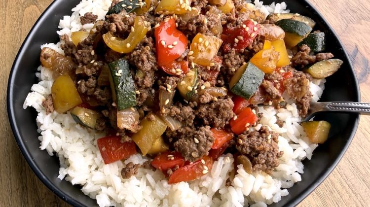 Cooked ground beef and bell pepper mixture over white rice in a bowl.