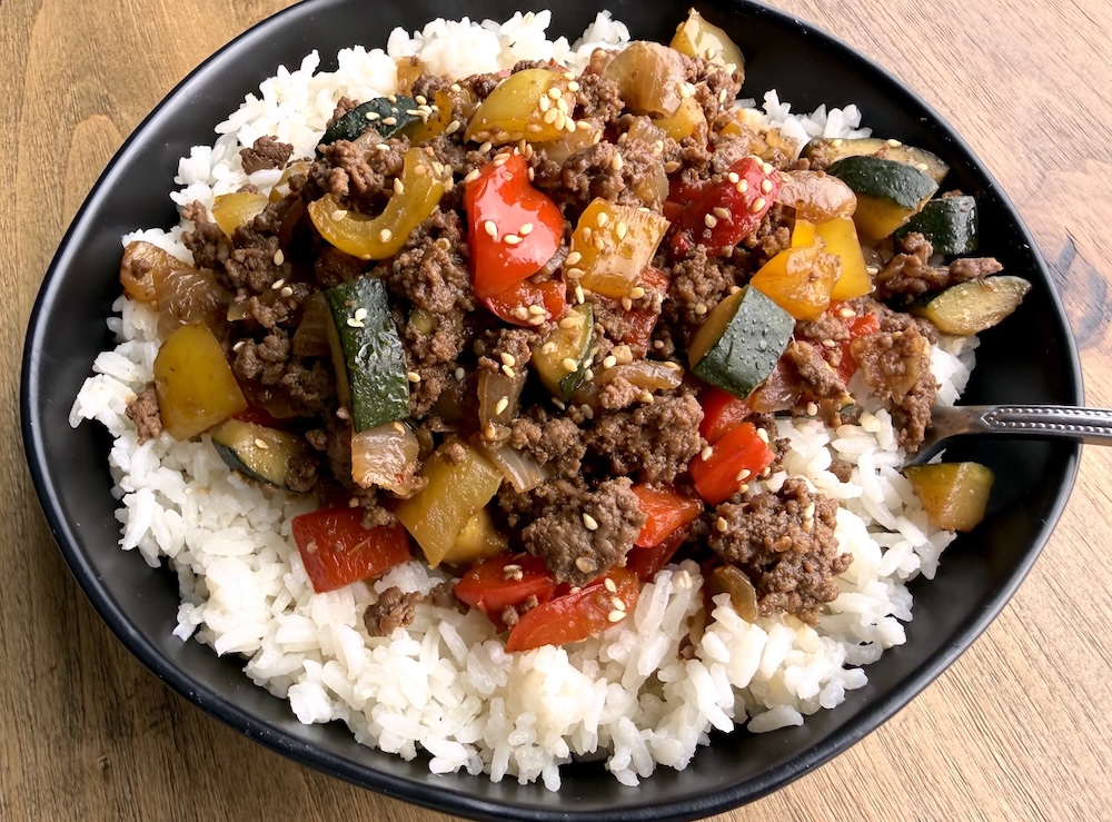 Cooked ground beef and bell pepper mixture over white rice in a bowl.