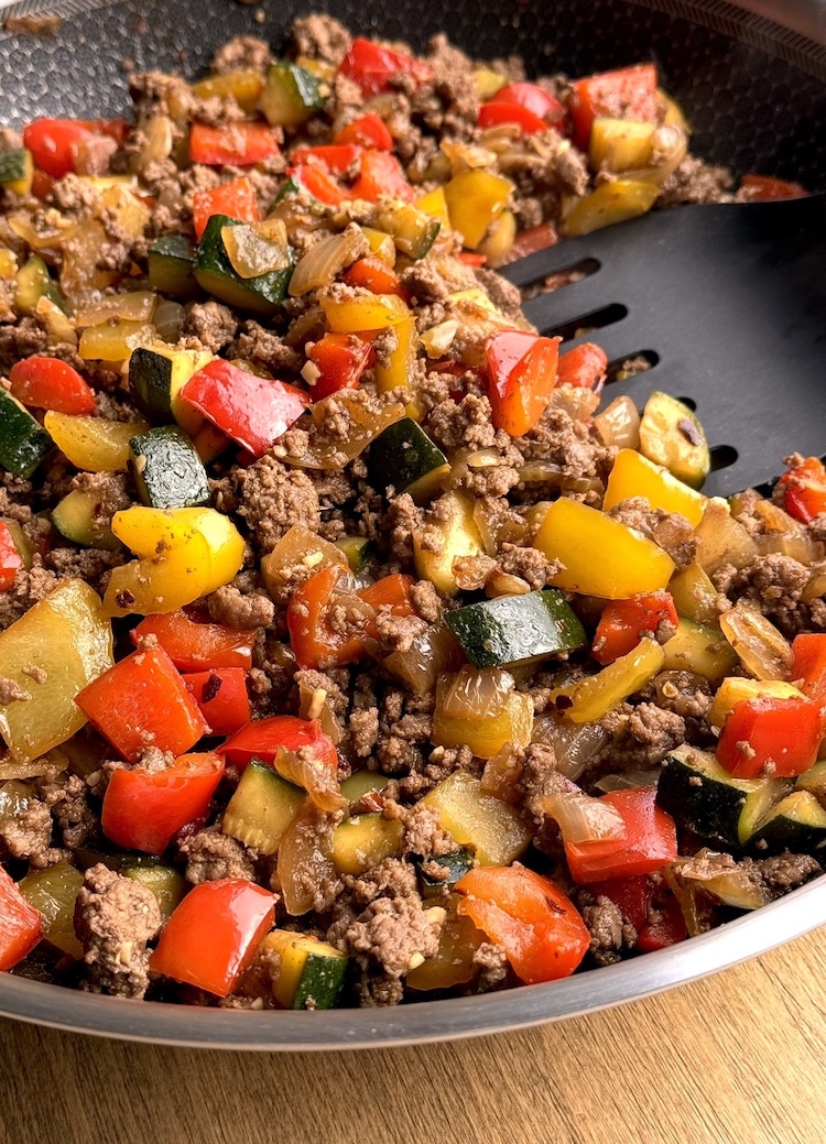 One pound of browned ground beef and colorful chopped bell peppers in a skillet.