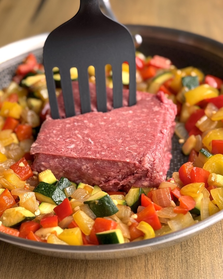 Large skillet filled with cooked bell peppers and onions with added raw ground beef for chopping and browning. 