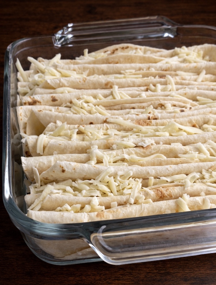 Folded flour tortillas in a glass baking dish stuffed with mozzarella cheese.