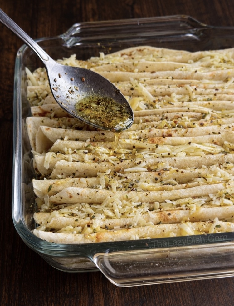 Folded flour tortillas in a glass baking dish being coated with a garlic her olive oil mixture.