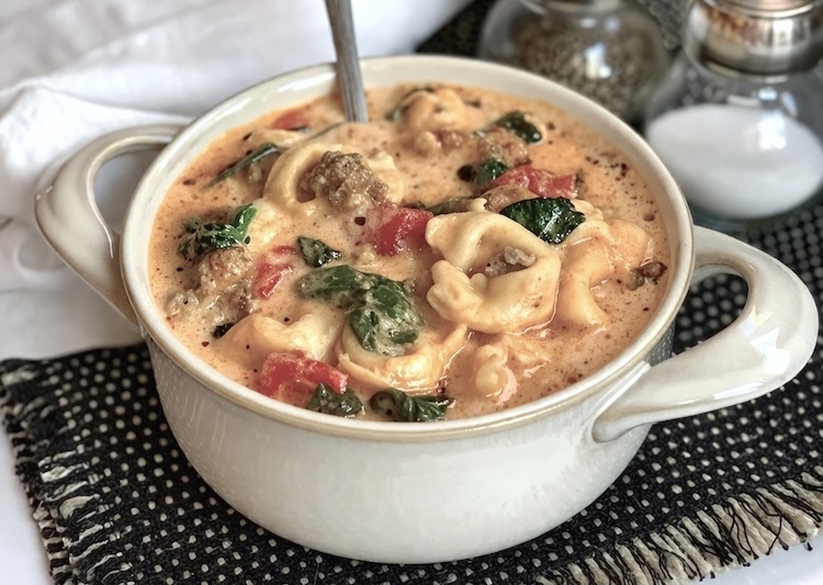 Close up view of a delicious and hearty creamy sausage pasta soup with spinach in a bowl. 