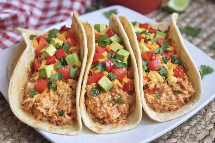 Close up view of 3 creamy salsa chicken tacos topped with avocado, cheddar, tomatoes, and cilantro. 