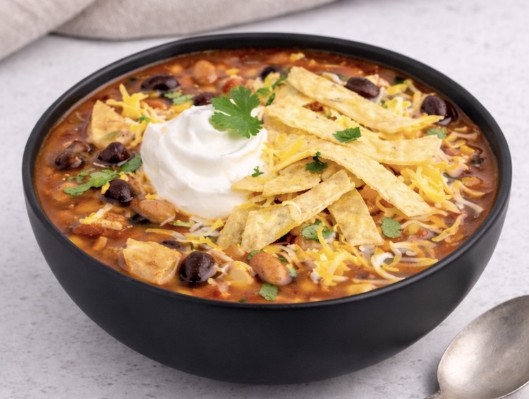 7 Can Chicken Taco Soup in a bowl topped with sour cream, cheese, and tortillas chips for a cheap and easy last minute dinner made with pantry staples. 
